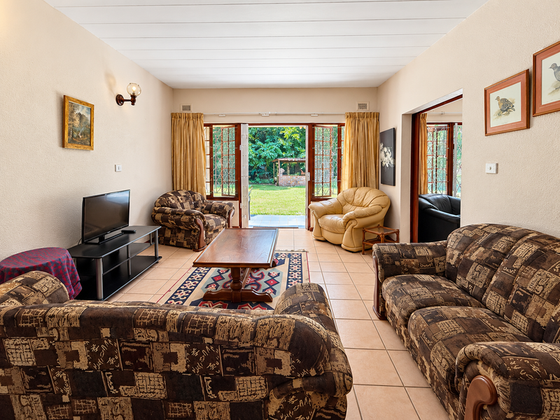 Spacious living room featuring tiled flooring and double glass doors that open directly onto a private garden area.