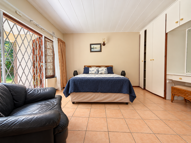 Spacious bedroom featuring built-in cupboards, a vanity area, tiled flooring, and direct access to an outdoor patio through a secure sliding door.