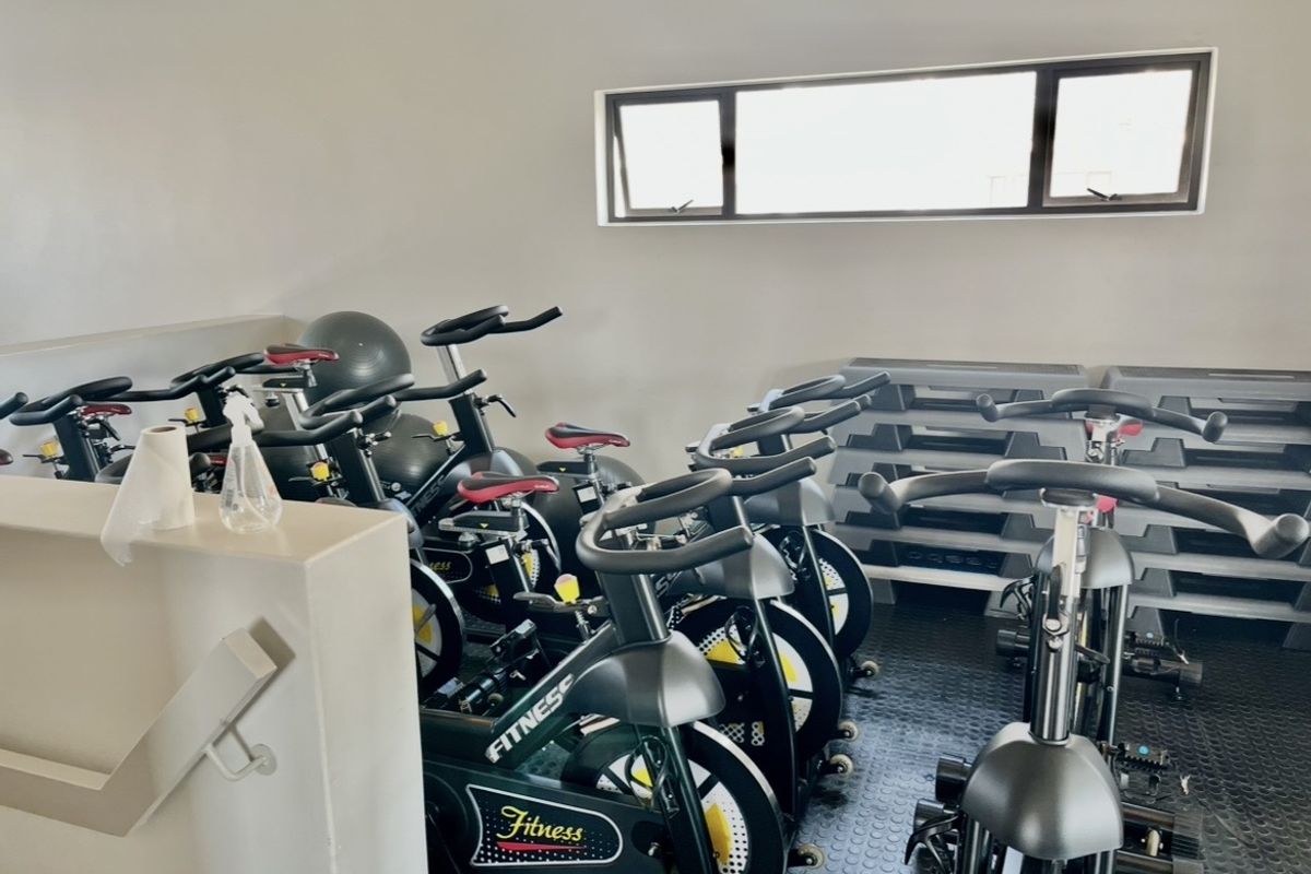 A functional gym space featuring durable rubber flooring and a horizontal awning window, equipped with multiple stationary exercise bikes.