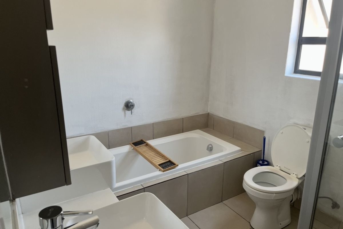 A functional bathroom featuring a built-in bathtub, tiled surround, basin with chrome mixer, and a standard toilet.