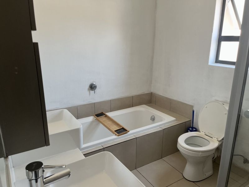 A functional bathroom featuring a built-in bathtub, tiled surround, basin with chrome mixer, and a standard toilet.