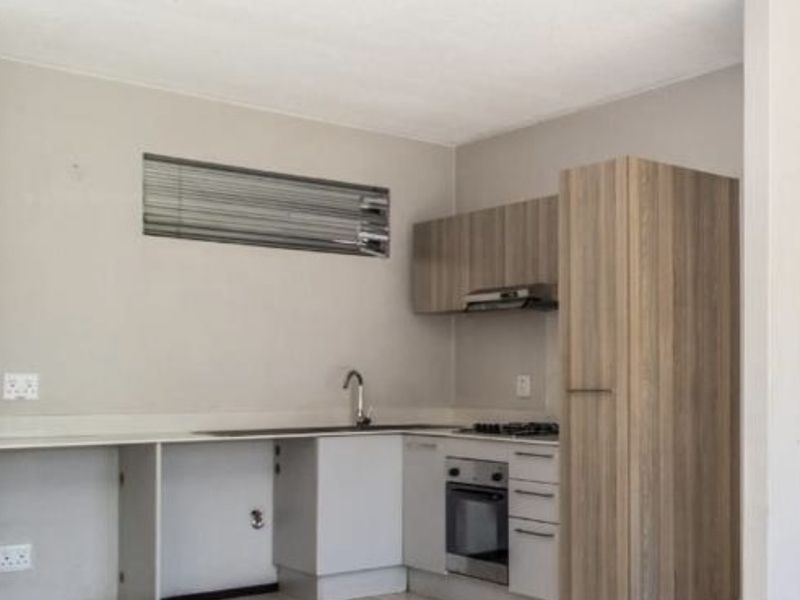 Compact kitchen featuring wood-look cabinetry, built-in oven, gas hob, and laminate flooring. The space is currently vacant and requires minor repairs to cabinetry.