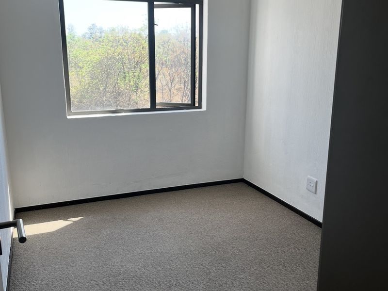 A clean, empty bedroom featuring neutral carpeting, white walls, and an aluminium-framed window providing natural light.