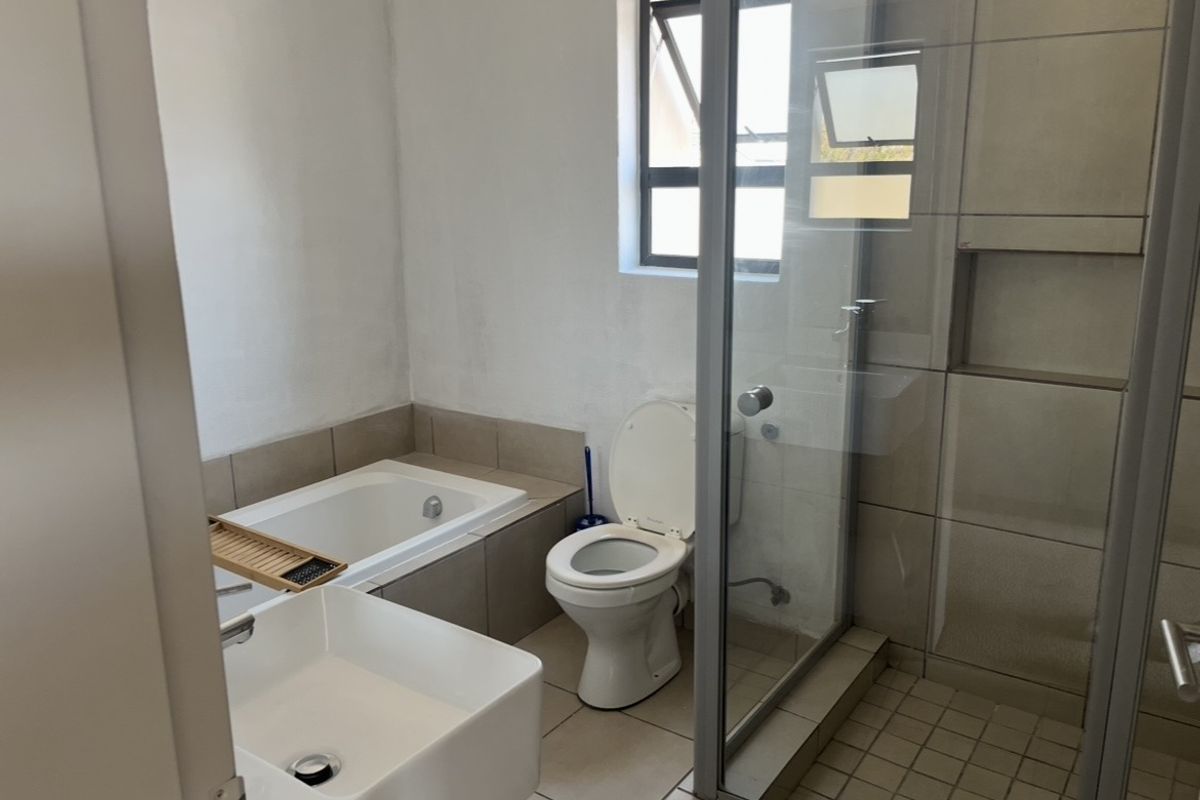 A functional bathroom featuring a built-in bathtub, separate glass shower enclosure, toilet, and basin with neutral tiling throughout.