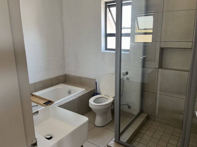 A functional bathroom featuring a built-in bathtub, separate glass shower enclosure, toilet, and basin with neutral tiling throughout.