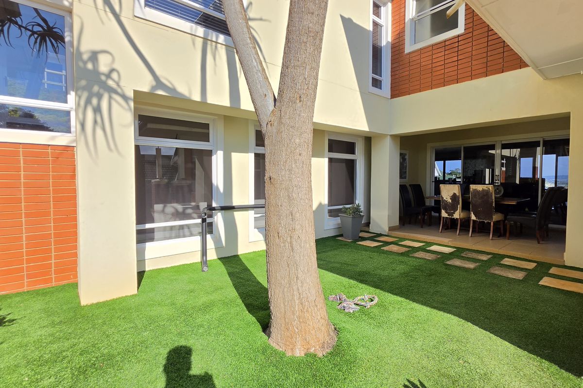 A well-maintained rear courtyard featuring artificial turf, paved stepping stones, and a covered patio area adjacent to the main living space.
