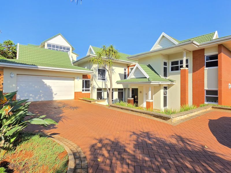Front elevation of a multi-level residential property featuring a paved driveway, double garage, and distinctive green tiled roof architecture.