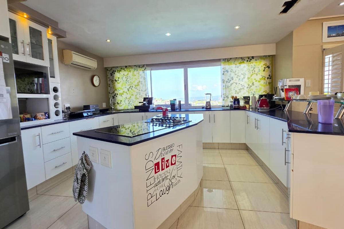 Spacious kitchen featuring a central island with a gas hob, ample white cabinetry, dark countertops, and tiled flooring with natural light.
