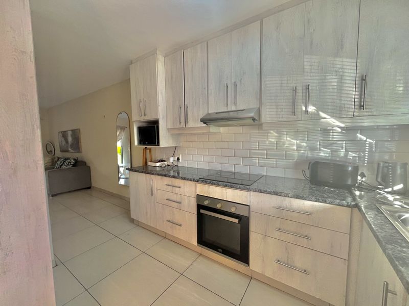 Modern kitchen featuring light wood-grain cabinetry, granite countertops, subway tile backsplash, and integrated stainless steel appliances, seamlessly flowing into the adjacent living area.