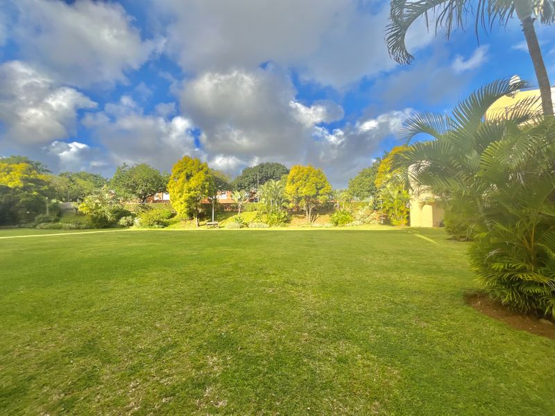 A well-maintained, expansive communal garden area featuring lush green lawns and mature trees within the apartment complex grounds.