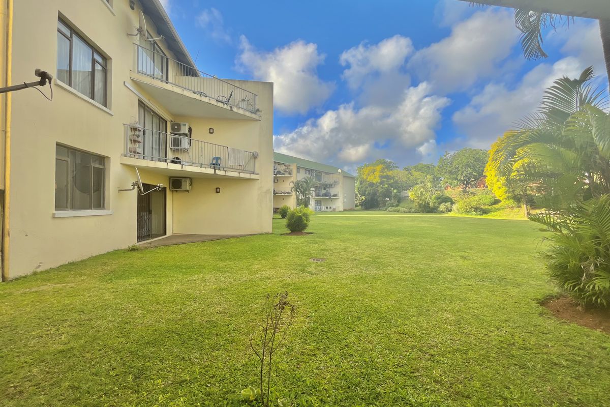 A view of the rear apartment facade featuring balconies, sliding glass doors, and well-maintained communal garden space.