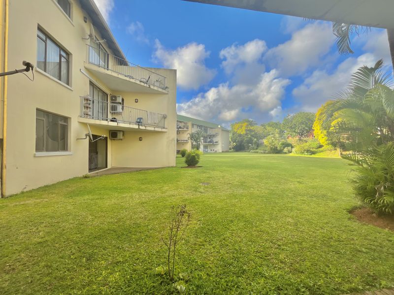 A view of the rear apartment facade featuring balconies, sliding glass doors, and well-maintained communal garden space.
