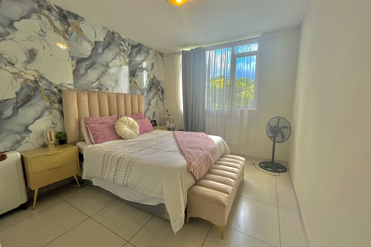 A well-maintained bedroom featuring large format floor tiles and a decorative marble-effect feature wall.