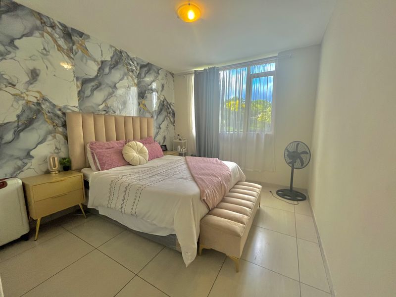 A well-maintained bedroom featuring large format floor tiles and a decorative marble-effect feature wall.