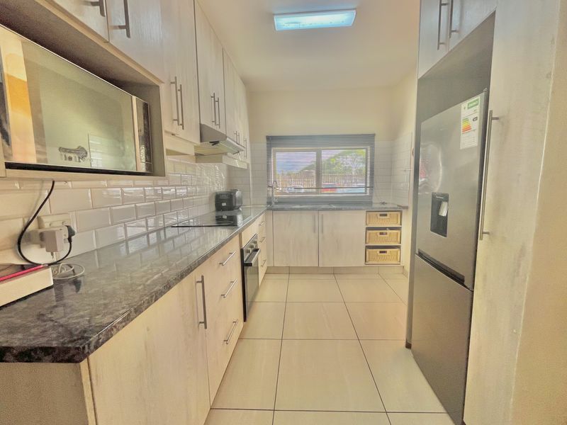 A well-maintained galley kitchen featuring light wood cabinetry, granite countertops, subway tile backsplash, and integrated appliances including an oven and hob.