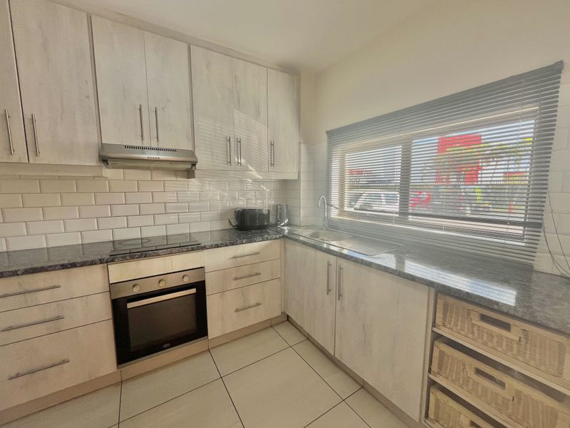 A functional kitchen featuring light wood-finish cabinetry, granite countertops, subway tile backsplash, and integrated appliances including an oven and hob.