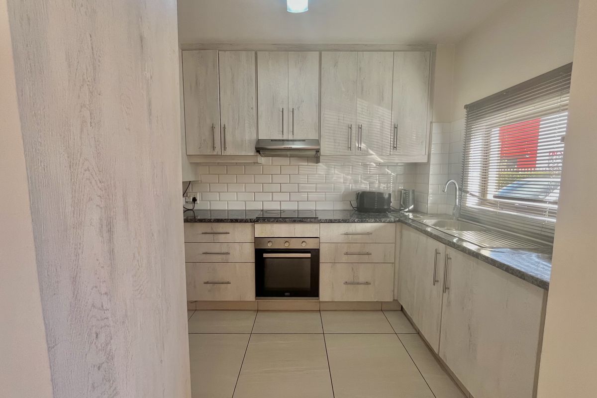 A functional kitchen featuring light wood-grain cabinetry, subway tile backsplash, integrated oven and hob, and tiled flooring with ample natural light.