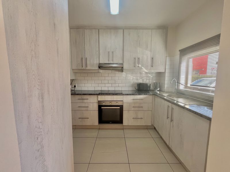 A functional kitchen featuring light wood-grain cabinetry, subway tile backsplash, integrated oven and hob, and tiled flooring with ample natural light.