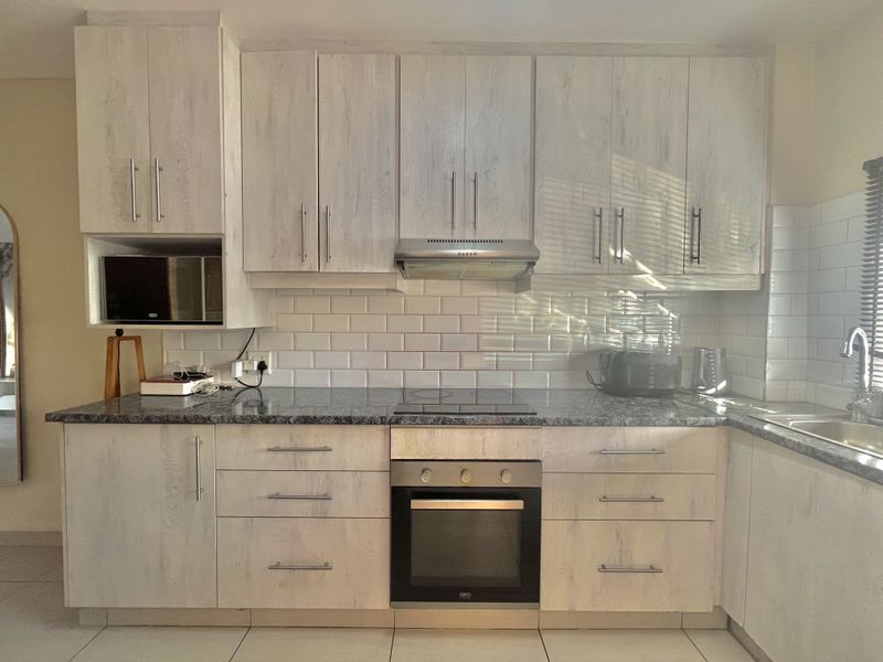 Modern kitchen featuring light wood-grain cabinetry, granite countertops, subway tile backsplash, and integrated stainless steel appliances including an oven and hob.