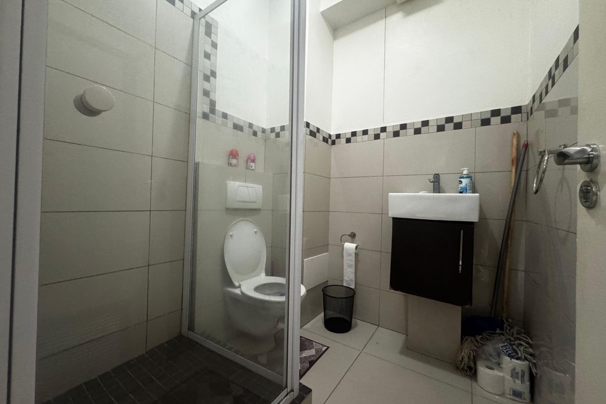 A compact bathroom featuring a glass-enclosed shower, wall-mounted toilet, and a small vanity basin with neutral tiled finishes.