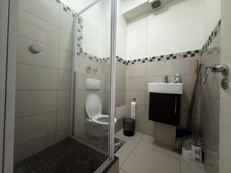 A compact bathroom featuring a glass-enclosed shower, wall-mounted toilet, and a small vanity basin with neutral tiled finishes.