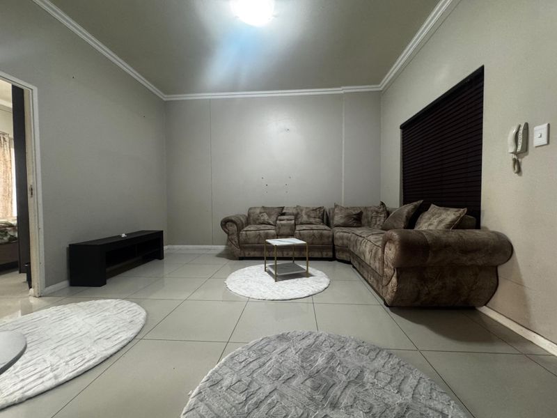 A spacious living room featuring neutral tiled flooring, crown molding, and an intercom system, offering a functional layout for relaxation.