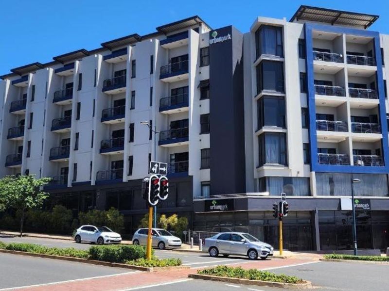 A modern multi-story apartment building featuring a contemporary facade with balconies and glass elements, situated on a corner lot with street access.