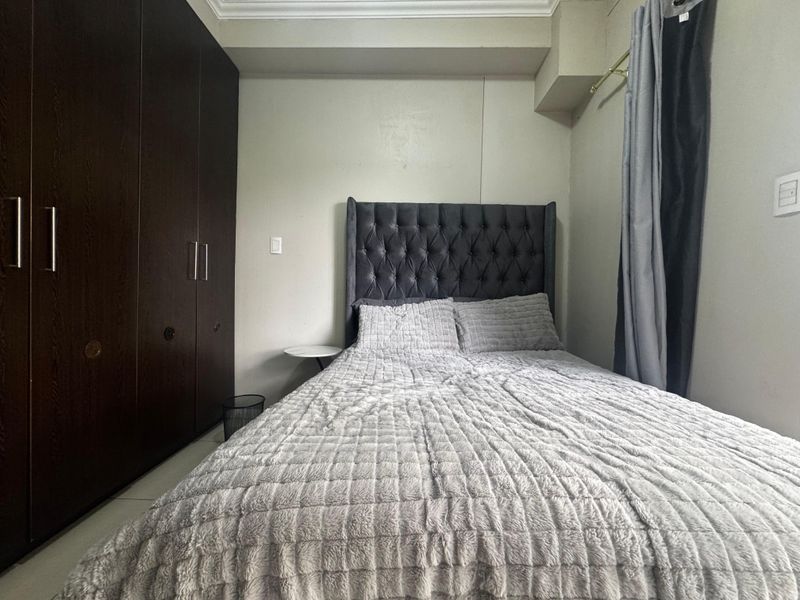 A bedroom featuring dark wood built-in wardrobes, tiled flooring, and decorative coving, providing a functional and compact sleeping space.
