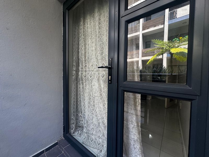 A view of an exterior balcony featuring modern dark aluminium framed glass doors and tiled flooring.