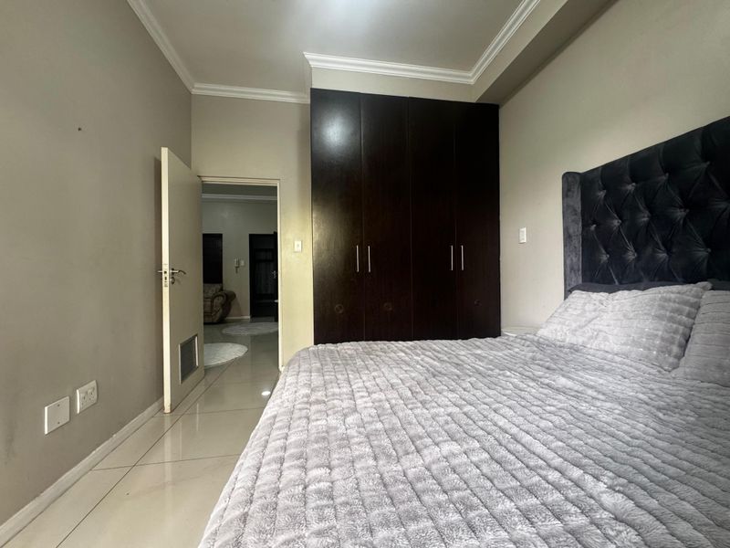 A well-maintained bedroom featuring dark wood built-in cupboards, neutral tiled flooring, and decorative ceiling cornicing.