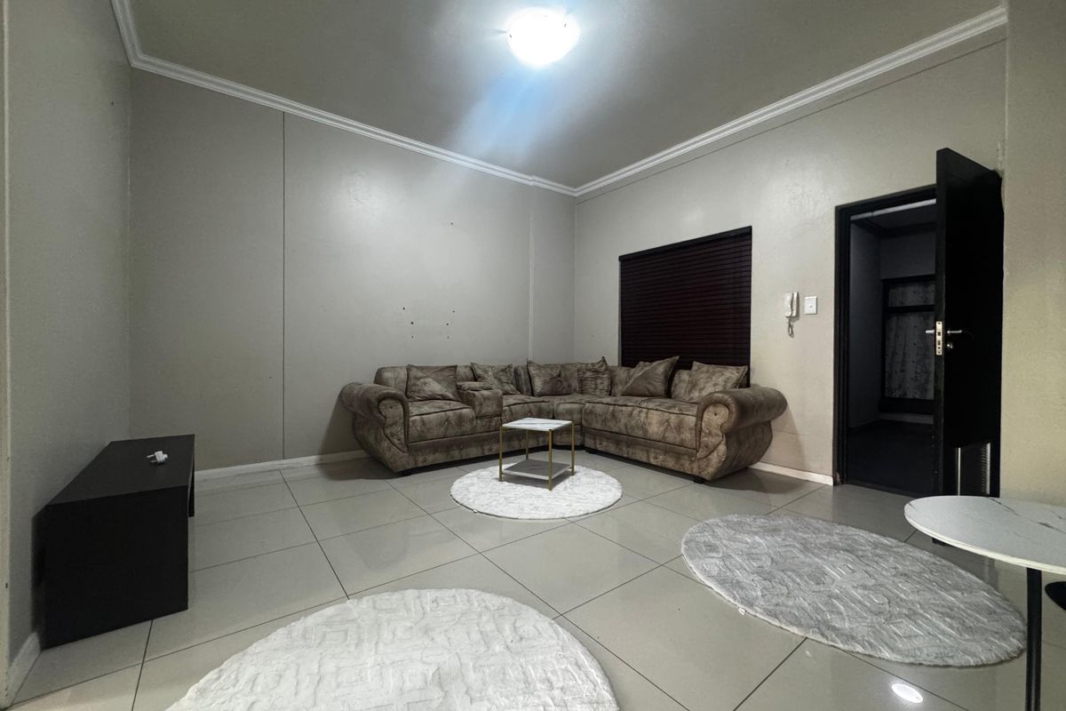 A spacious living room featuring neutral tiled flooring, cove cornicing, and an intercom system, providing a functional base for comfortable living.
