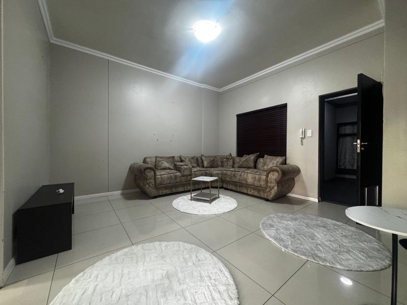 A spacious living room featuring neutral tiled flooring, cove cornicing, and an intercom system, providing a functional base for comfortable living.
