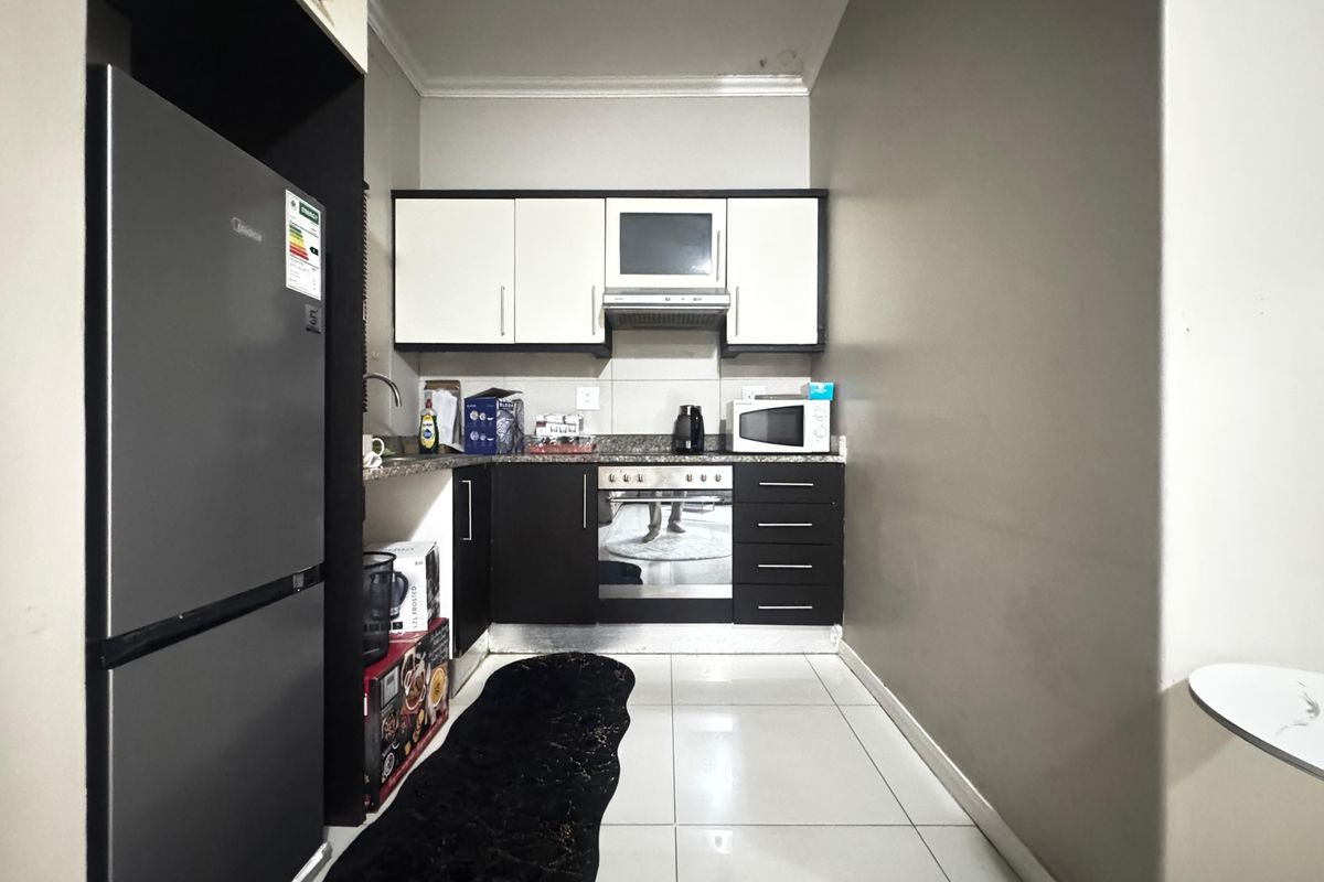 Compact kitchen featuring modern two-tone cabinetry, granite countertops, built-in oven, and extractor fan, finished with tiled flooring.