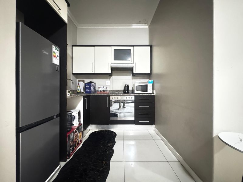 Compact kitchen featuring modern two-tone cabinetry, granite countertops, built-in oven, and extractor fan, finished with tiled flooring.