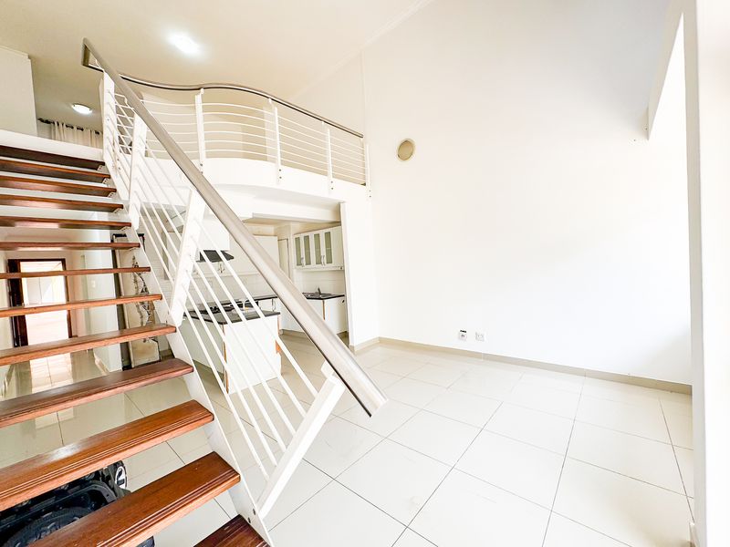 Spacious open-plan living area featuring a modern staircase leading to a mezzanine level, with an integrated kitchen and neutral tiled flooring throughout.