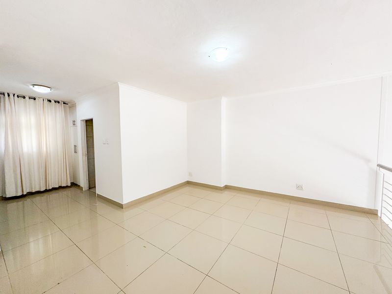 A bright, open-plan living area featuring neutral tiled flooring, clean white walls, and a built-in storage cupboard.