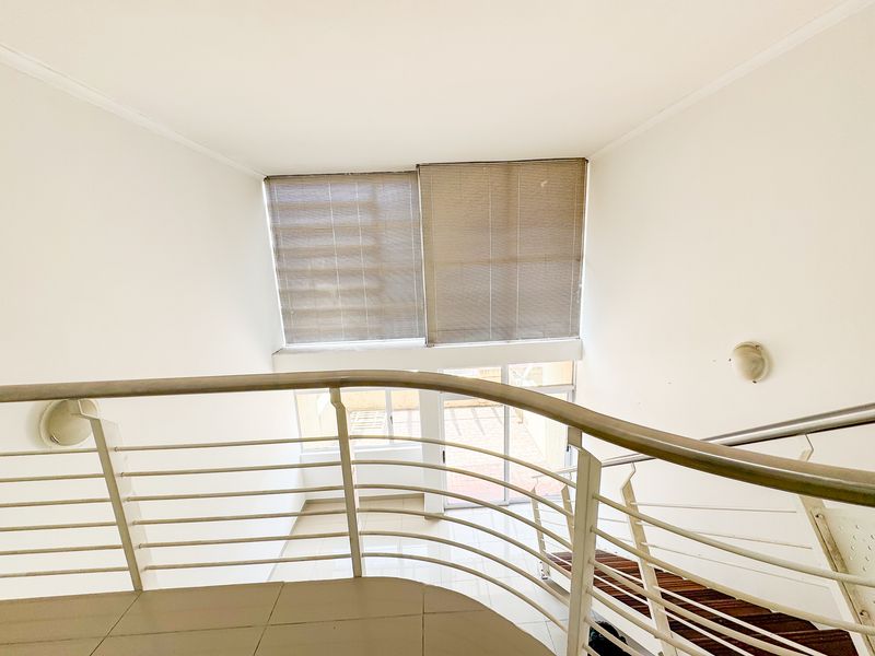 A bright landing area featuring a curved metal balustrade overlooking the lower level, with tiled flooring and large windows fitted with blinds.