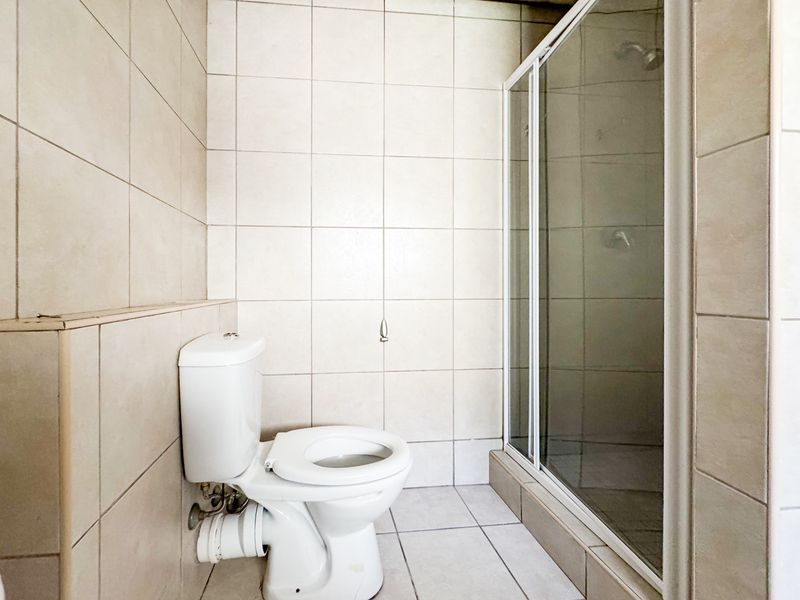 A functional bathroom featuring a standard toilet and a glass-enclosed shower with neutral wall and floor tiling.