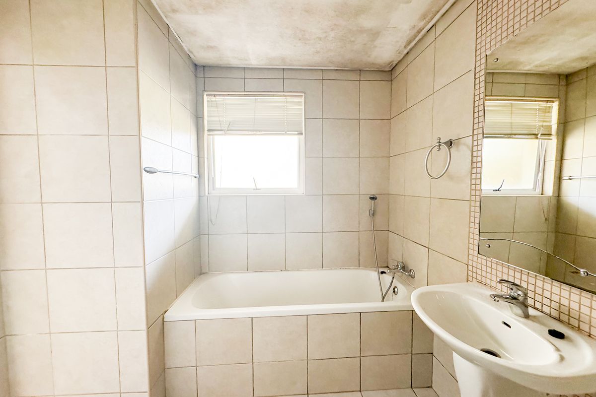 A functional bathroom featuring a built-in bathtub, pedestal basin, and tiled finishes. The ceiling shows signs of water damage requiring repair.