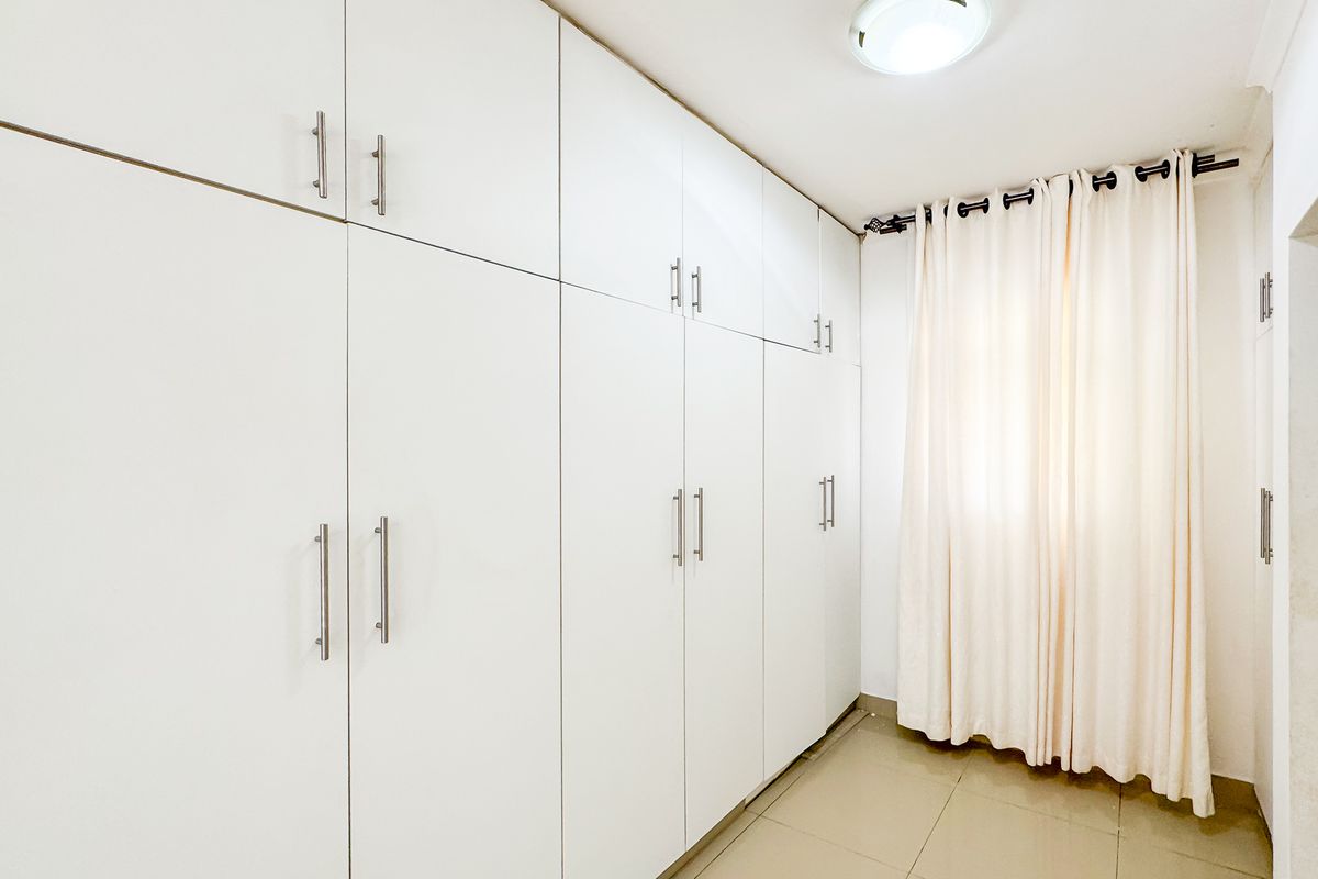 A clean, empty bedroom featuring extensive white built-in cupboards, neutral tiled flooring, and a simple ceiling light fixture.