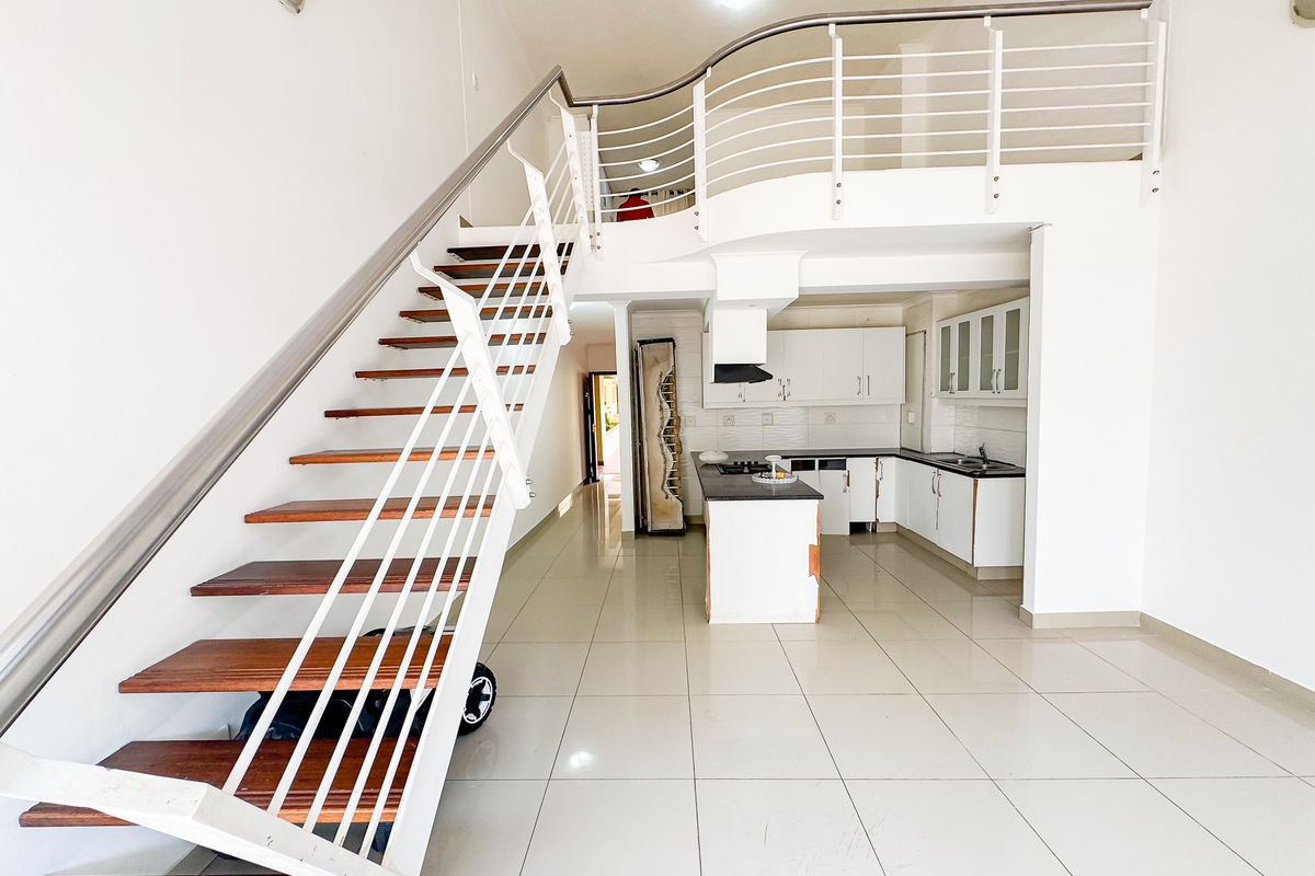Open-plan living area featuring a modern staircase, mezzanine level, and a functional kitchen with built-in cabinetry and island.