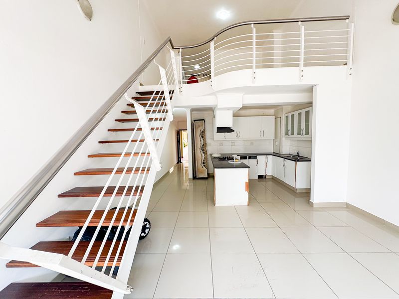 Open-plan living area featuring a modern staircase, mezzanine level, and a functional kitchen with built-in cabinetry and island.