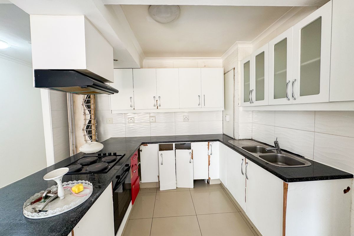 A functional kitchen featuring black granite countertops, built-in cabinetry, and integrated appliances, currently requiring some maintenance and cosmetic repairs to cabinet doors.