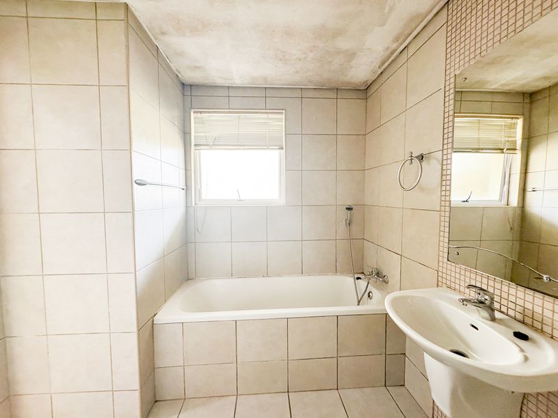 A functional bathroom featuring a built-in bathtub, pedestal basin, and tiled finishes. The ceiling shows signs of water damage requiring repair.