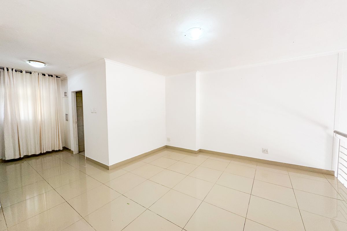 A bright, open-plan living area featuring neutral tiled flooring, clean white walls, and a built-in storage cupboard.