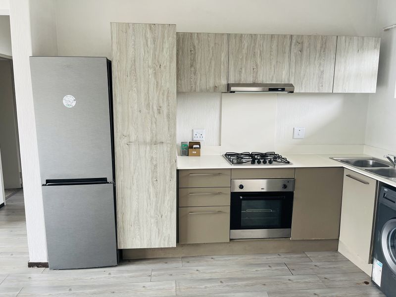 Modern kitchen featuring wood-look upper cabinetry, neutral lower cabinets, gas hob, built-in oven, extractor fan, and durable laminate flooring.