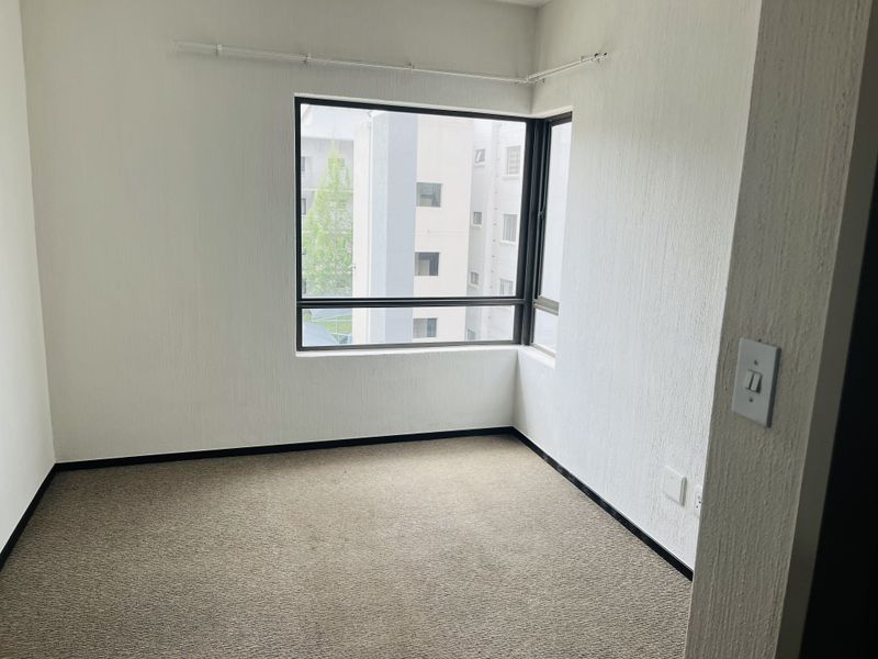 An empty bedroom featuring textured walls, carpeted flooring, and a corner window providing natural light and an urban view.