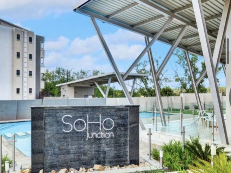 A modern communal pool area featuring a sleek metal pergola, glass balustrades, and a prominent stone feature wall within a well-maintained apartment complex.