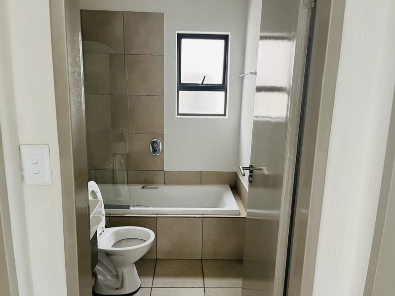 A clean and functional bathroom featuring a built-in bathtub with a glass shower screen, tiled finishes, and a toilet.