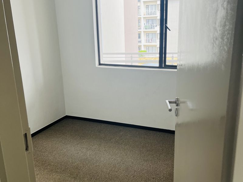 An empty bedroom featuring neutral walls, carpet flooring, and a large window with an aluminium frame.